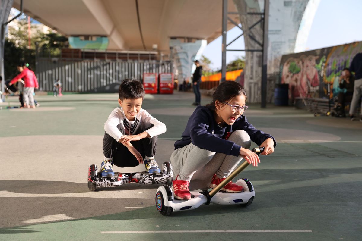 Two children riding hoverboard go-kart attachments in a skate park