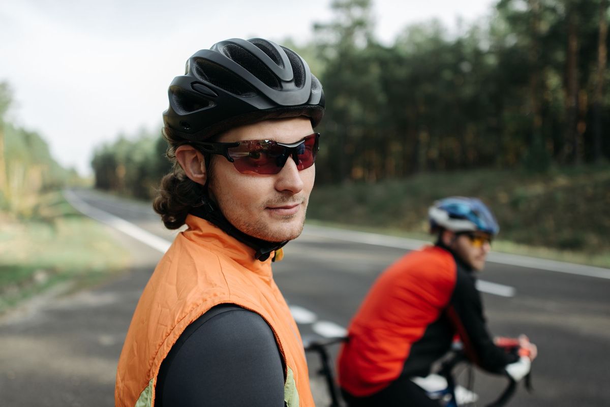 Two cyclists enjoying a sunny ride on a forest road, wearing helmets and sunglasses