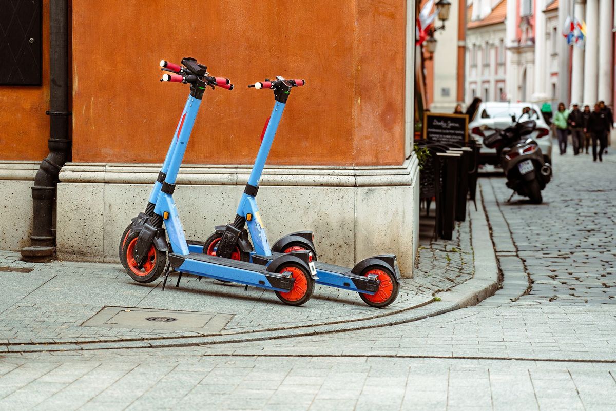 Two electric scooters parked by a historic wall in Poznań, Poland on a cobblestone street