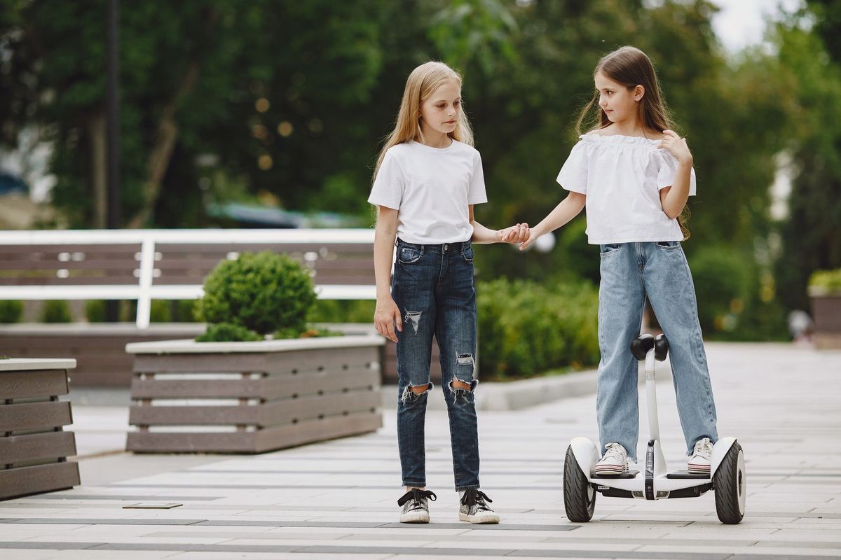 Two girls holding hands, one riding a self-balancing scooter in a park
