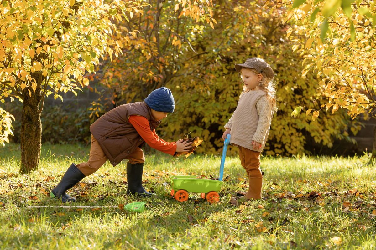 Two kids enjoy a playful autumn day in the garden with a cart and leaves