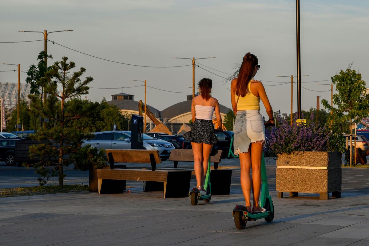 Two women ride electric scooters in Tallinn, Estonia during a golden sunset