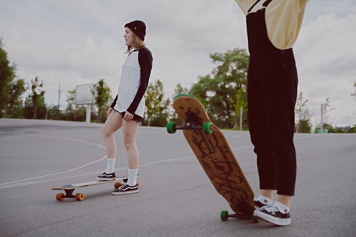 Two young women with longboards in an open area, embodying streetwear fashion and friendship