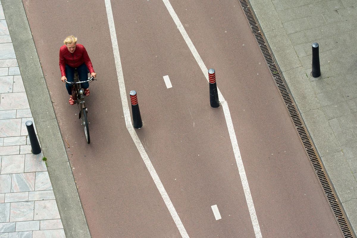 Woman cycling in an urban bike lane seen from above, flanked by bollards