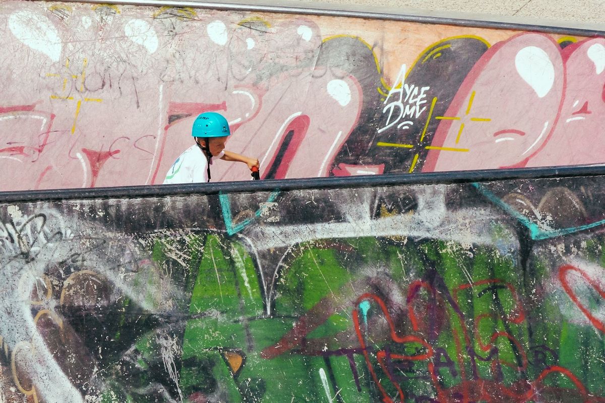 Young boy on a scooter navigating a colorful, graffiti-adorned skatepark under daylight