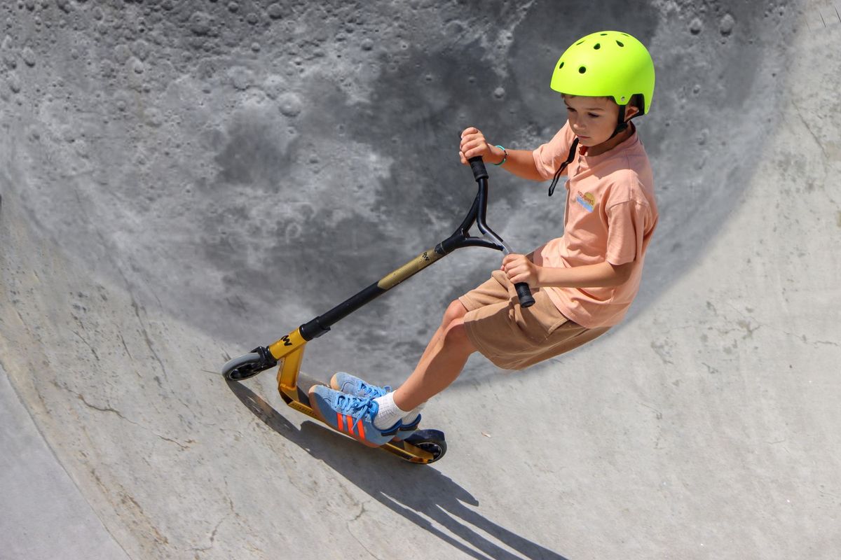 Young boy wearing a helmet riding a scooter on a ramp at a skate park in Granville, Normandie, France
