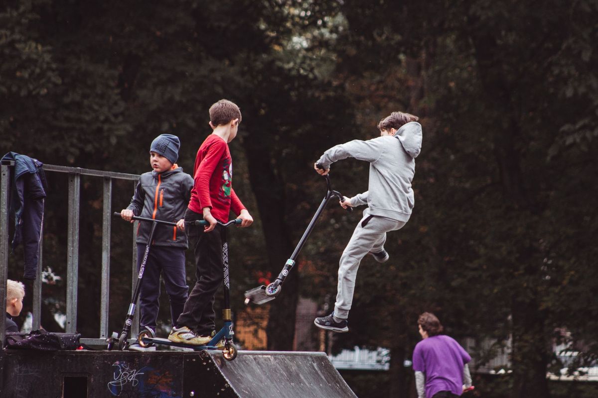 Young boys enjoying and performing tricks on kick scooters at an outdoor skate park