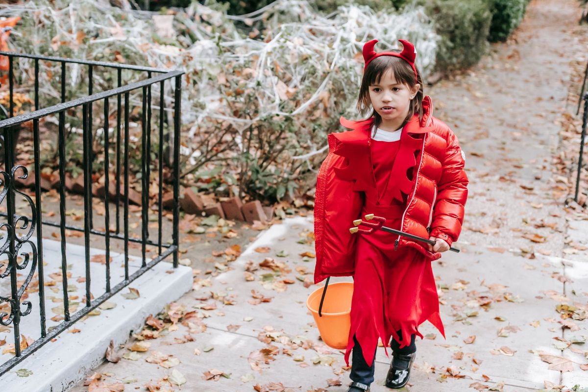 Young girl dressed as a devil with a red costume and bucket walking on a fall day outdoors