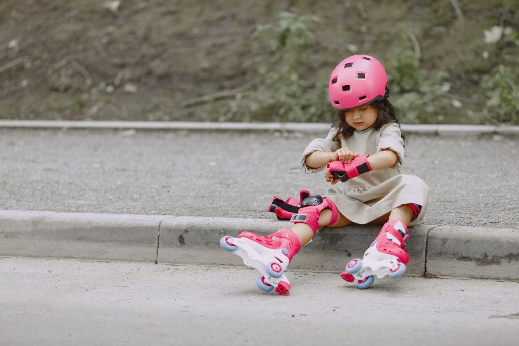 Young girl in rollerblades and helmet sitting on a curb, ready to skate outdoors
