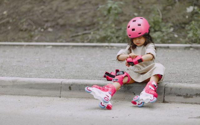 Young girl in rollerblades and helmet sitting on a curb, ready to skate outdoors