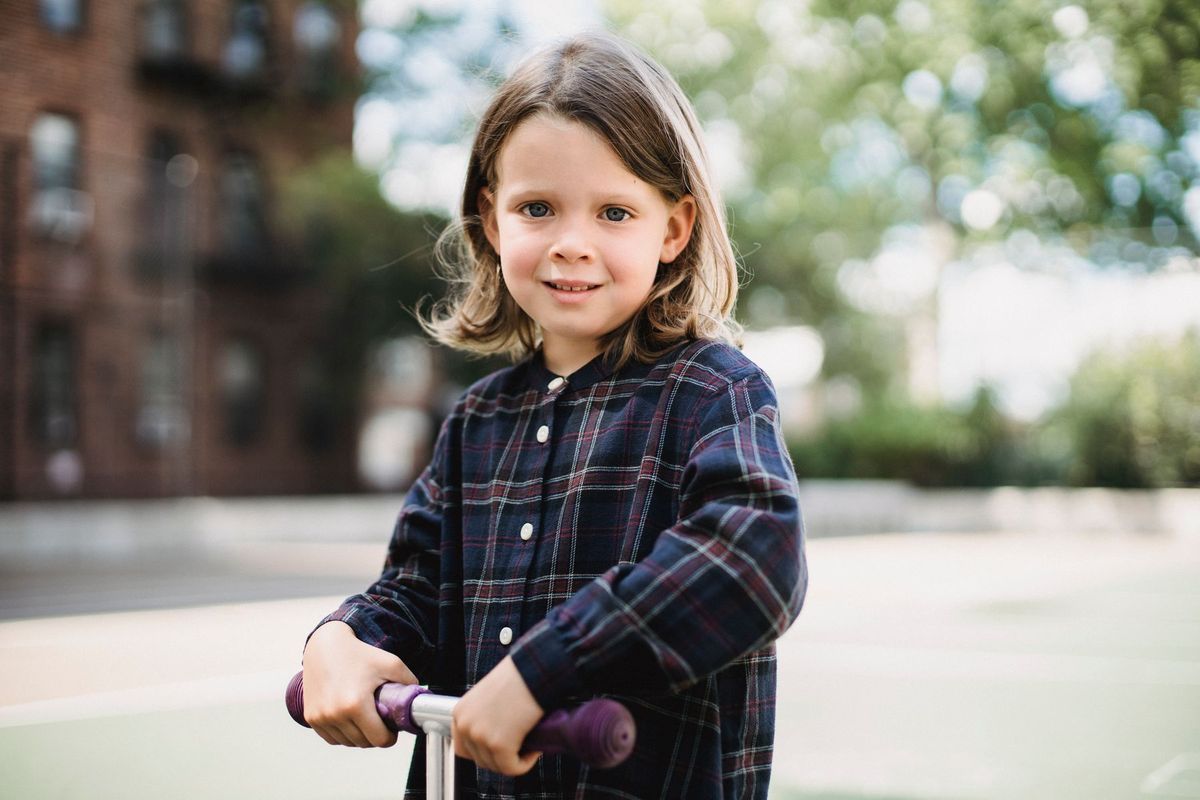 Young girl smiling while riding a scooter in a sunny urban playground