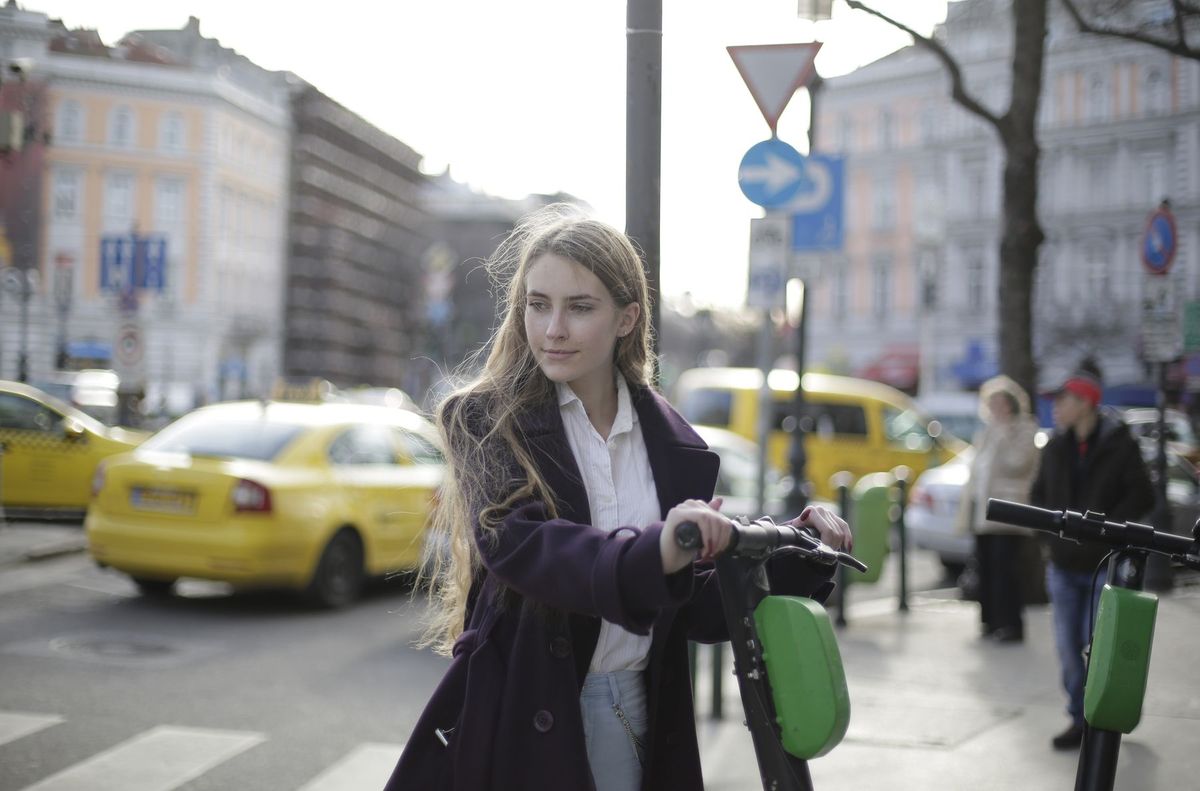 Young woman with long hair riding an electric scooter on a busy city street