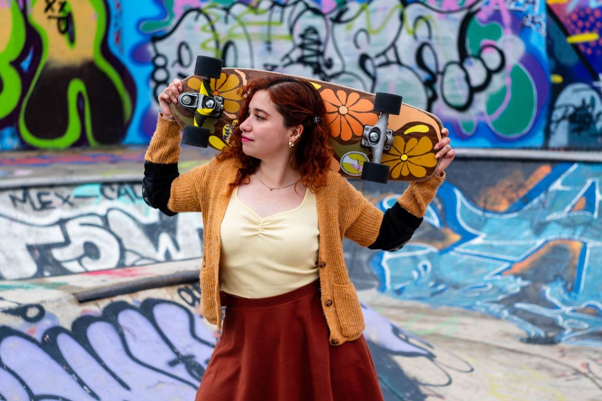 Young woman with skateboard rests by colorful graffiti at an urban skatepark